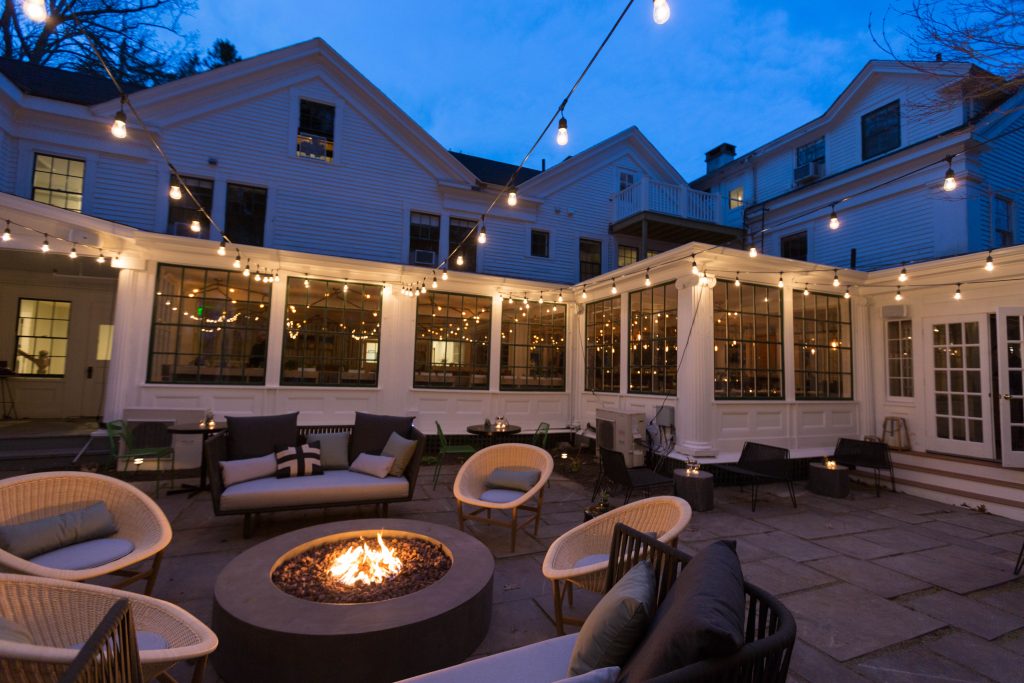Outdoor patio with a firepit, seating, and twinkle lights at dusk. Photo Credit: Rarebrick Photography