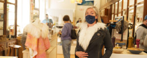 Woman in mask trying on coat at Maine Craft Portland, Photo Courtesy of Good Maine