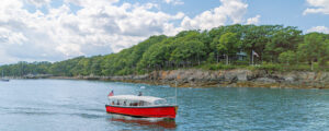 red boat sailing past green island on blue water; Photo Credit: Peter G. Morneau Photography