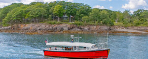 red boat sailing past green island on blue water; Photo Credit: Peter G. Morneau Photography