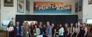 Group posing under 'Welcome to Maine" sign; Photo Credit: Digital Edge
